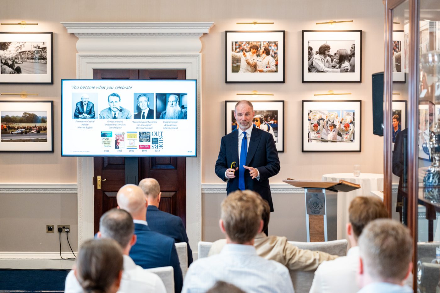 Brett Kelly presenting to shareholders at the 2026 meetup in Pall Mall, London, in front of a slide titled You become what you celebrate.